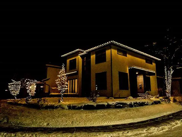 Warm white roofline lights and light-wrapped trees on a two-storey home